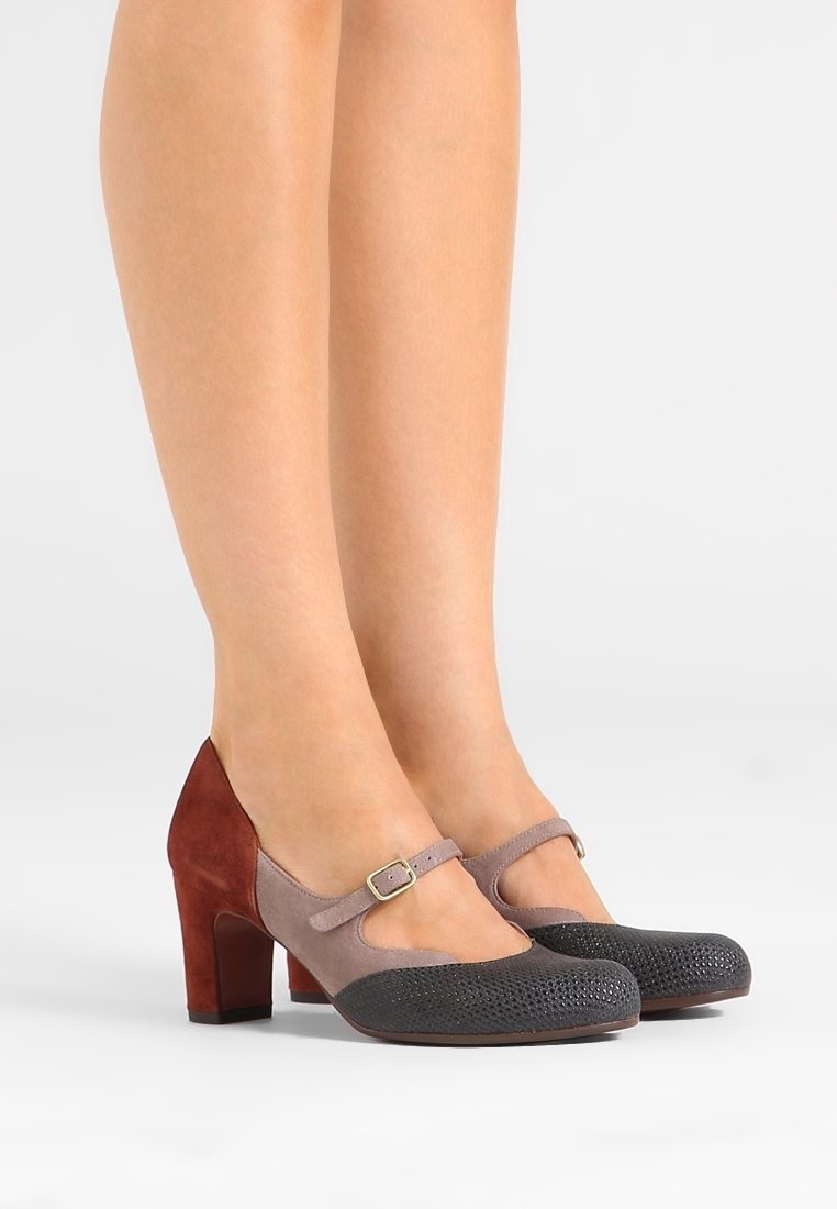 Chaussures à talons Mary Jane bicolores pour femmes, avec bout texturé noir, bride taupe et talon bloc en suède rouge foncé, portées sur jambes nues.