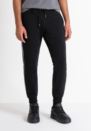 Pantalones de chándal negros hechos de tela suave, con un ajuste tapered, puños elásticos, cintura con cordón y rayas blancas en los lados.