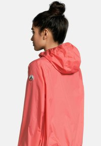 Giacca impermeabile rosa con cappuccio, dotata di una patch con logo sulla manica e una texture liscia e lucida.