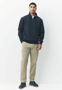 Marine kwart-zip sweatshirt, beige chino's en zwarte schoenen met tan zolen. Casual pasvorm met ribgebreide manchetten en een gladde textuur.