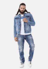 Hellblaues Denim-Jackett mit weißem Kunstfellkragen, durchgehende Knopfleiste, zwei Brusttaschen, kombiniert mit hellblauen Jeans und weißen Sneakers.