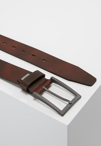 Brauner Leder Gürtel mit einer matten grauen Metallschnalle, ausgestattet mit mehreren Löchern zur Anpassung und einer glatten Textur.