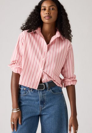 Roze overhemd met dunne rode strepen, opgerolde mouwen en een ontspannen pasvorm. Gecombineerd met high-waisted blauwe jeans en een zwarte riem.
