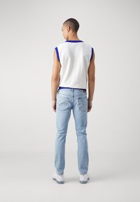 Camiseta sin mangas blanca con ribete azul, combinada con jeans de un azul claro. Los jeans tienen un corte clásico y detalles visibles en los bolsillos traseros.