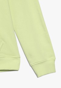 Manga de sudadera verde claro hecha de un suave tejido texturizado con puño acanalado, que presenta un diseño sin costuras y sin logotipos o patrones visibles.