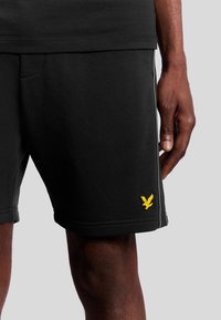 Pantaloni sportivi neri in cotone, con ricamo del logo giallo e cuciture laterali con dettagli grigio chiaro.