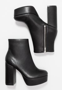 Botas de tobillo de cuero negro con un alto tacón cuadrado, detalle de cremallera y puntera redondeada. Textura suave con suela de plataforma.