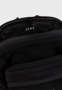 Svart DKNY-väska med en slät nylonutsida, överdel med dragkedja och tygfoder. Inuti finns en varumärkesetikett.