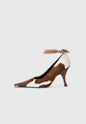 Brown and white cow print high heel shoe with a pointed toe, textured surface, and an ankle strap with a light brown buckle.