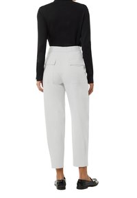 Lichtgrijze broek met elastische tailleband, zijzakken en een tapered leg ontwerp. Draagt een aansluitend zwart longshirt en zwarte schoenen.