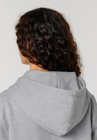 Felpa grigia con cappuccio realizzata in un tessuto morbido. Il cappuccio presenta un design arrotondato e il tessuto appare liscio con un leggero motivo melangiato.