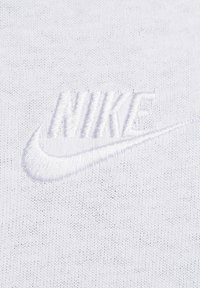 Vitt broderat Nike-logotyp med swoosh på en vit stickad tygbakgrund, som framhäver textur och sömnadsdetaljer.