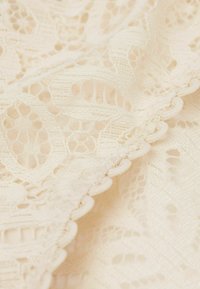 Spets tyg i elfenben med intrikata blommönster och texturerad detaljering. Kanten är försedda med en scalloped trim för en extra design.