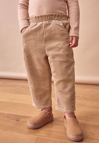 Beige corduroybukser med lodrette ribber, elastisk talje, sidelommer og blomsterbroderi. Sættes sammen med beige slip-on sko.