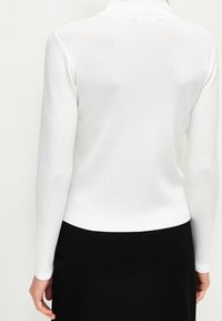 Pull à col roulé blanc à manches longues en maille texturée. Coupe légèrement cintrée avec une finition lisse et un minimum de détails.