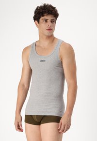 Top sin mangas gris con canalé y escote redondo, que presenta el logo de Versace en negro, combinado con unos pantalones cortos verdes oliva. Tejido de algodón suave.