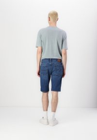 Světle šedé tričko, modré džínové šortky s pěti kapsami a bílé tenisky. Šortky mají ohrnutý okraj a hnědou koženou nášivku na pásku.