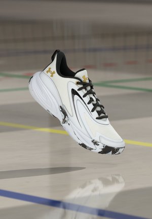 Weißer Sportschuh mit schwarzen und goldenen Akzenten, schwarzen Schnürsenkeln und marmorierter Sohle, der über einem Indoor-Sportboden schwebt.