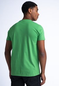 Camiseta de algodón verde con mangas cortas, cuello redondo y una textura suave. La vista trasera muestra un diseño limpio y simple sin patrones.