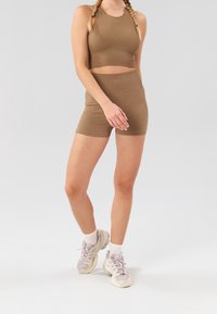 Haut court côtelé marron et short taille haute assorti. Le modèle porte des baskets gris clair et beige avec des chaussettes blanches. Design simple, texture douce.