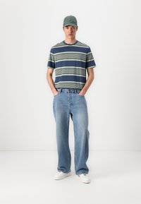 Ribaga T-särk tumesinises ja rohelises, koos heledate siniste laia säärega teksadega. Roheline müts ja valged sneekerid täiendavad riietust.