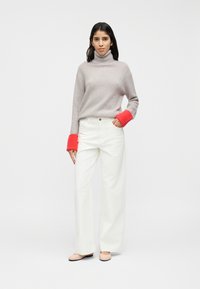 Γκρι πουλόβερ ζιβάγκο με κόκκινες μανσέτες, συνδυασμένο με άσπρο παντελόνι φαρδιάς γραμμής και ανοιχτά καφέ μπαλαρίνες. Απλός, μίνιμαλ σχεδιασμός με απαλή υφή.