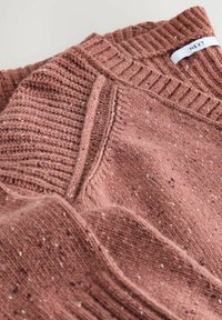 Texturierter, gestrickter Pullover in sanftem Rosaton mit einem gerippten Ausschnitt und gesprenkeltem Muster. Das Etikett trägt die Aufschrift "NEXT."