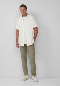 Kortegesleeve lichtcrème shirt met twee borstzakken, gecombineerd met olijfgroene broeken en witte sneakers met beige accenten. Eenvoudig ontwerp.