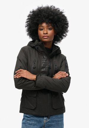 Black softshell jacket with a hood, featuring elastic drawstrings, zippered and flap pockets, and a logo detail on the front.