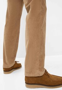 Tan corduroy broek met smalle verticale ribbels, gecombineerd met bruine suède schoenen met een lage profiel en vetersluiting.