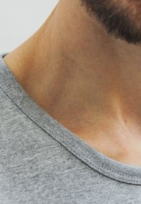 Grijze katoenen t-shirt met een geribde ronde hals, vertonend een gladde textuur en subtiele kleurvariatie. Focus op de nek- en schouderzone.