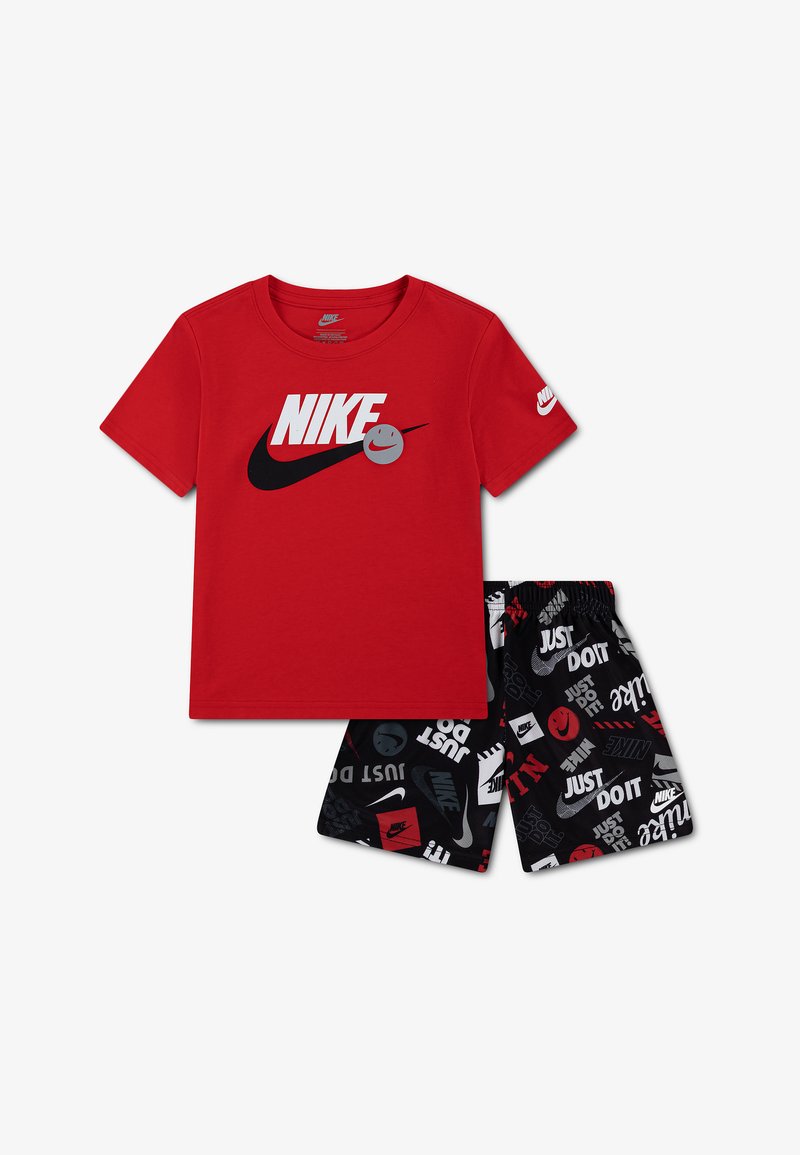 Κόκκινο κοντομάνικο μπλουζάκι Nike με μαύρο λογότυπο Swoosh και χαμογελαστό πρόσωπο, συνδυασμένο με μαύρο σορτς που διαθέτει λευκά και κόκκινα λογότυπα Nike και το κείμενο "Just Do It".