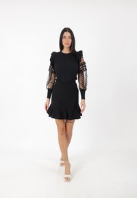 Vestido negro con un corsé ajustado y mangas abullonadas de tela transparente. La falda tiene un diseño acampanado y un dobladillo con volantes.