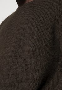 Pullover marrone a maglia con un collo alto e un motivo a coste testurizzato. Il tessuto sembra morbido e caldo, adatto per il clima fresco.