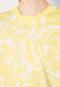 Närbild på en person som bär en skjorta med svart och vit marmorering, med gul krage och en liten vit "BOSS"-logotyp på bröstet.