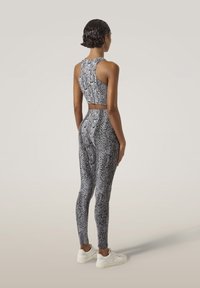 Top de sport court imitant le serpent noir et blanc et leggings, avec une coupe ajustée et une texture lisse, associés à des baskets blanches.