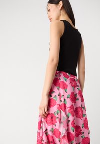 Haut sans manches noir associé à une jupe florale rose ornée de grandes roses rouges et de feuilles vertes, mettant en avant un design fluide et superposé.