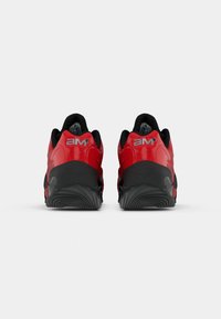 Zapatillas deportivas rojas con suela negra, que presentan un material superior suave y un talón acolchado con la marca en la parte trasera.