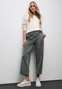 Light beige knitted sweater with a textured pattern, paired with tailored green trousers featuring side pockets and a loose fit, completed with white sneakers.