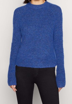 Person wearing a long-sleeve, blue knitted sweater paired with black pants, shown from shoulders to hips against a plain background.
