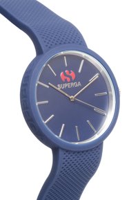 Reloj de silicona azul con una carátula redonda, manos y marcadores plateados. Presenta una correa texturizada y un prominente logo rojo, "SUPERGA."