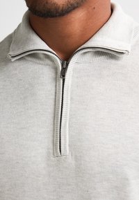 Felpa zip grigia chiara con colletto a coste e tessuto texturizzato. Caratterizzata da una cerniera metallica sul davanti, design aderente.