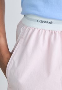 Světle růžové šortky s měkkou texturou, které mají bílý elastický pas s logem "Calvin Klein" v elegantním černém písmu.