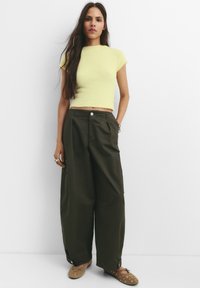 Világos sárga, rövid ujjú kötött felső és laza, olíva zöld, magas derekú nadrág zsebekkel. Barna slip-on cipők dekoratív részletekkel.