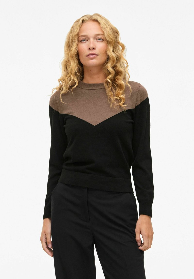 Pull coloré en noir et marron avec un col rond, présentant un motif en chevrons à l'avant et des manches longues. Texture douce.