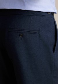 Pantalons bleu marine en tissu texturé avec une poche arrière et fermeture à bouton. Présentent un devant plat et une coupe ajustée pour un look contemporain.