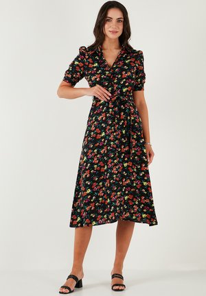 Floral dress with a black background, featuring short puff sleeves, a collared neckline, waist tie, and a flowing mid-length skirt.