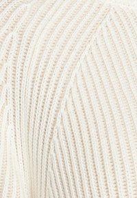 Gestrickter cremfarbener Pullover mit einem gerippten Muster, der diagonale Streifen und ein weiches, voluminöses Aussehen aufweist.