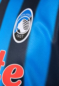 Atalanta fotballtrøye med vertikale blå og svarte striper, teksturert stoff, rød logotekst og et sirkulært lagemblem med profilmotiv.