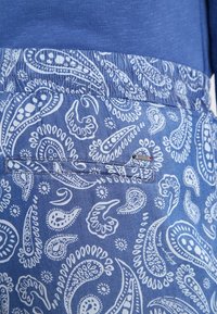 Tissu bleu avec un motif paisley blanc, doté d'une taille élastique et d'un petit accent décoratif près de la poche.